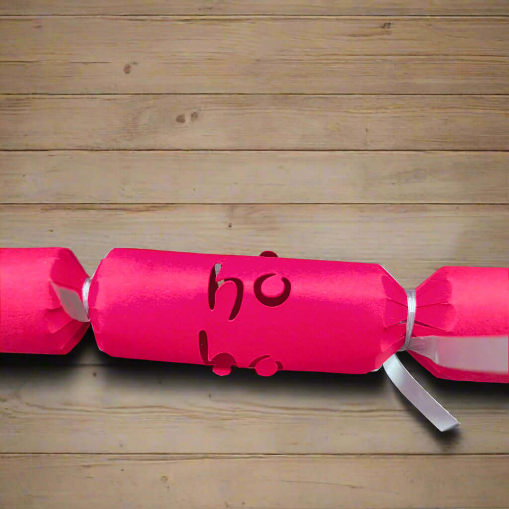 Close-up of red Christmas cracker with “Ho Ho” cut-out detail, tied with silver ribbon, placed on a wooden table for scale.