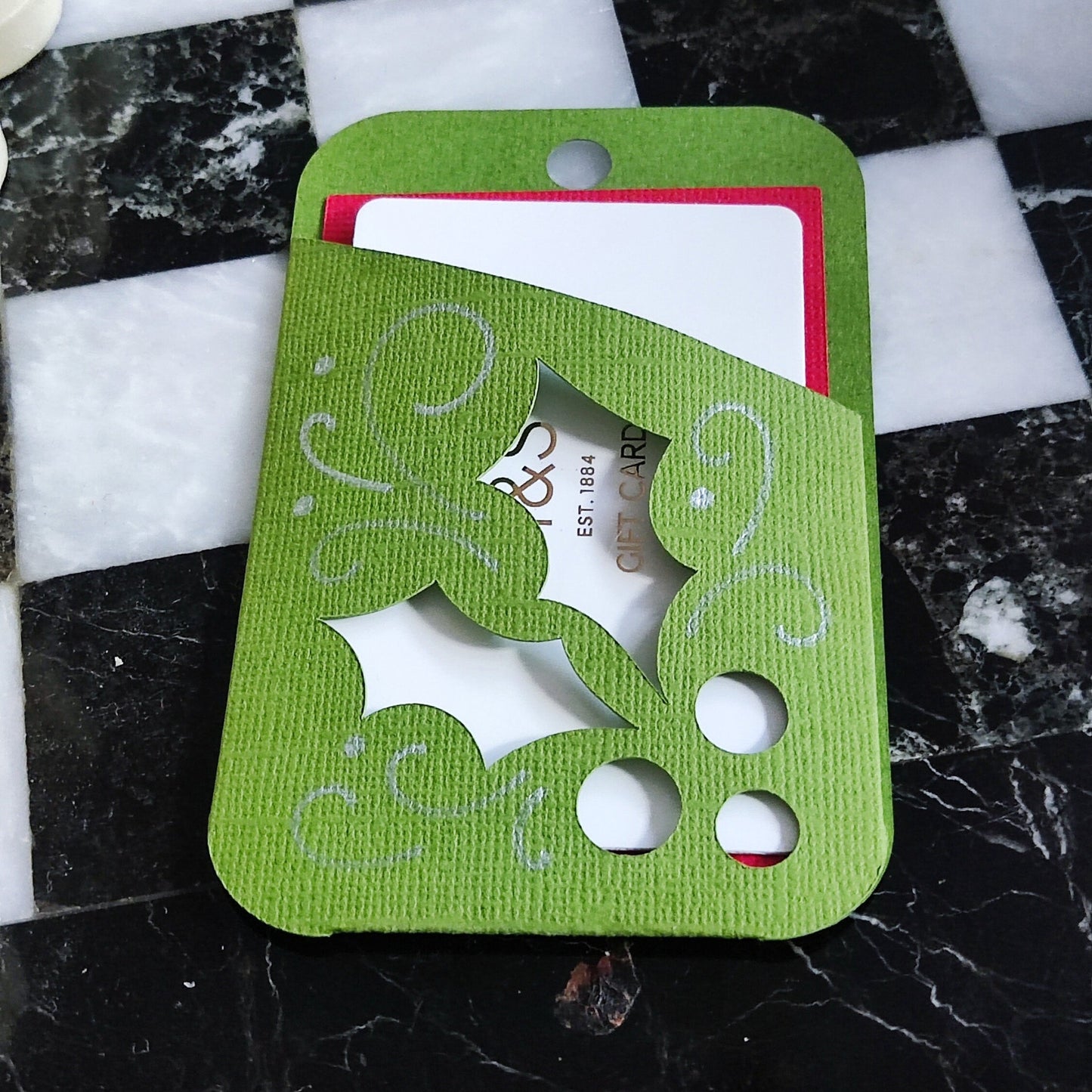 Green and red Christmas gift card holder with holly design, perfect for presenting gift cards during the holiday season.