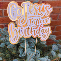 Detailed view of a gold and white “Go Jesus It’s Your Birthday” party decoration with sticks for display.