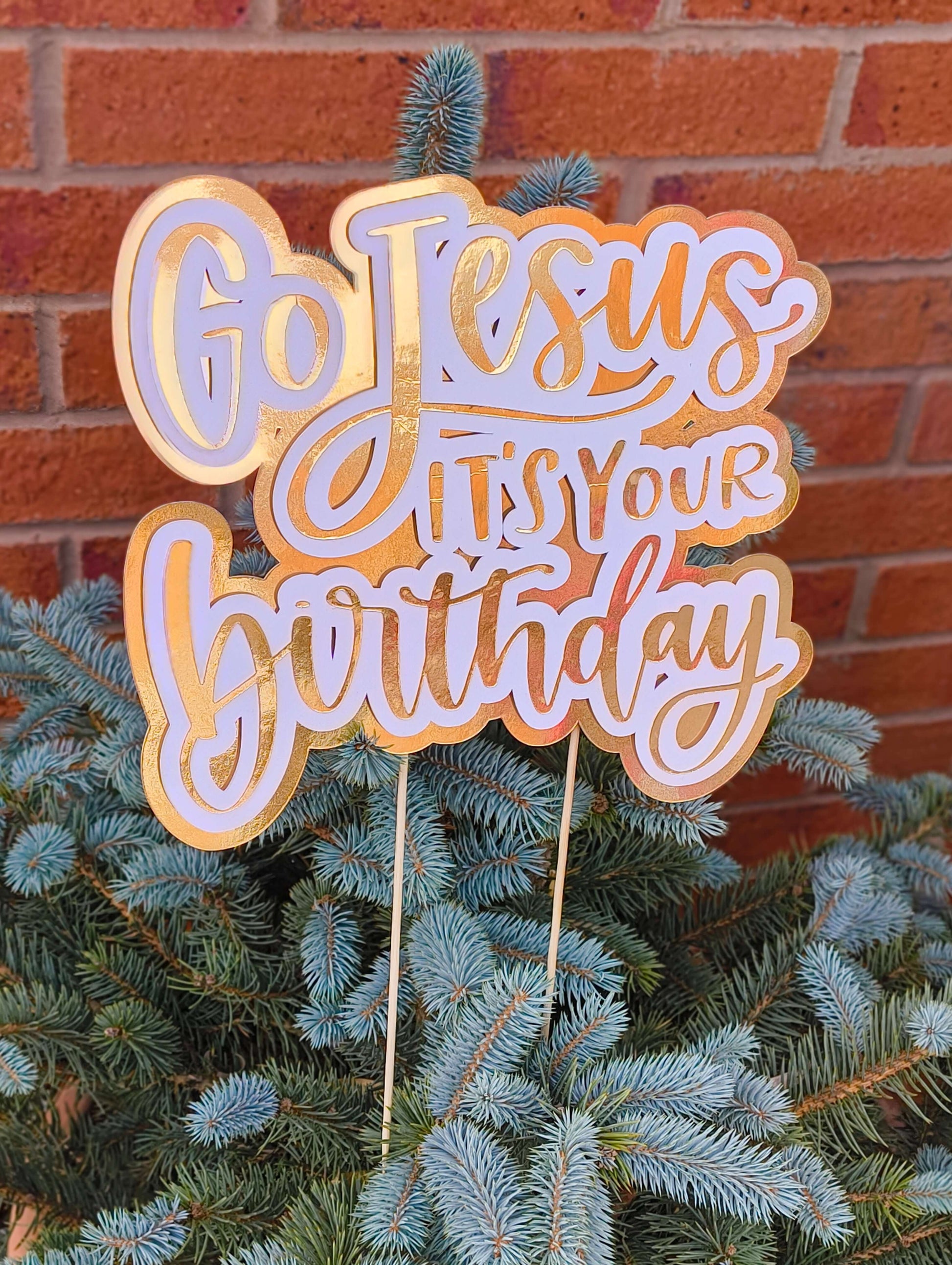 Detailed view of a gold and white “Go Jesus It’s Your Birthday” party decoration with sticks for display.