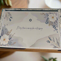 Jewish sympathy card with Star of David and floral border, text reads 'May their memory be a blessing', soft pastel design on wooden surface