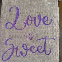 Rustic jute-style drawstring pouch featuring “Love is Sweet” in sparkling purple glitter. Compact size, ideal for sweets, favours, or small keepsakes.