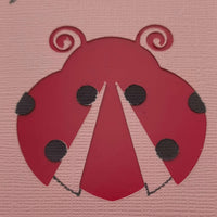 Close-up detail of a handmade red ladybird embellishment on pink textured cardstock, part of a greeting card design ideal for birthdays or well wishes.