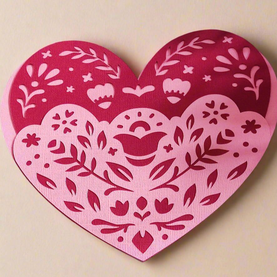 Layered heart papercut with folk floral design in pink and red tones, flat-lay angle on cream background, perfect for Valentine's Day or romantic gifts