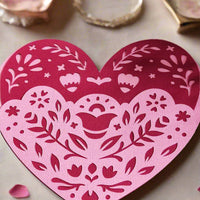 Layered heart papercut in pink and red with floral folk design, styled flat-lay on soft beige surface with rose petals and trinket dishes, a romantic handmade gift