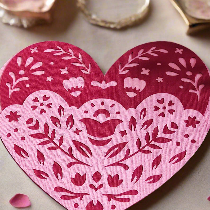 Layered heart papercut in pink and red with floral folk design, styled flat-lay on soft beige surface with rose petals and trinket dishes, a romantic handmade gift