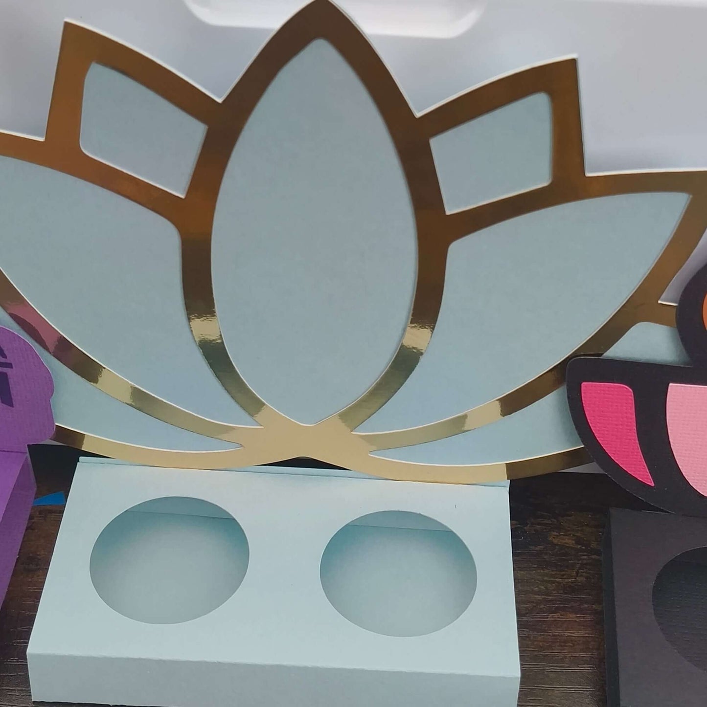 Front-facing close-up of a mint green Diwali sweet holder with an elegant gold foil lotus design, made from layered cardstock, displayed on a wooden surface.
