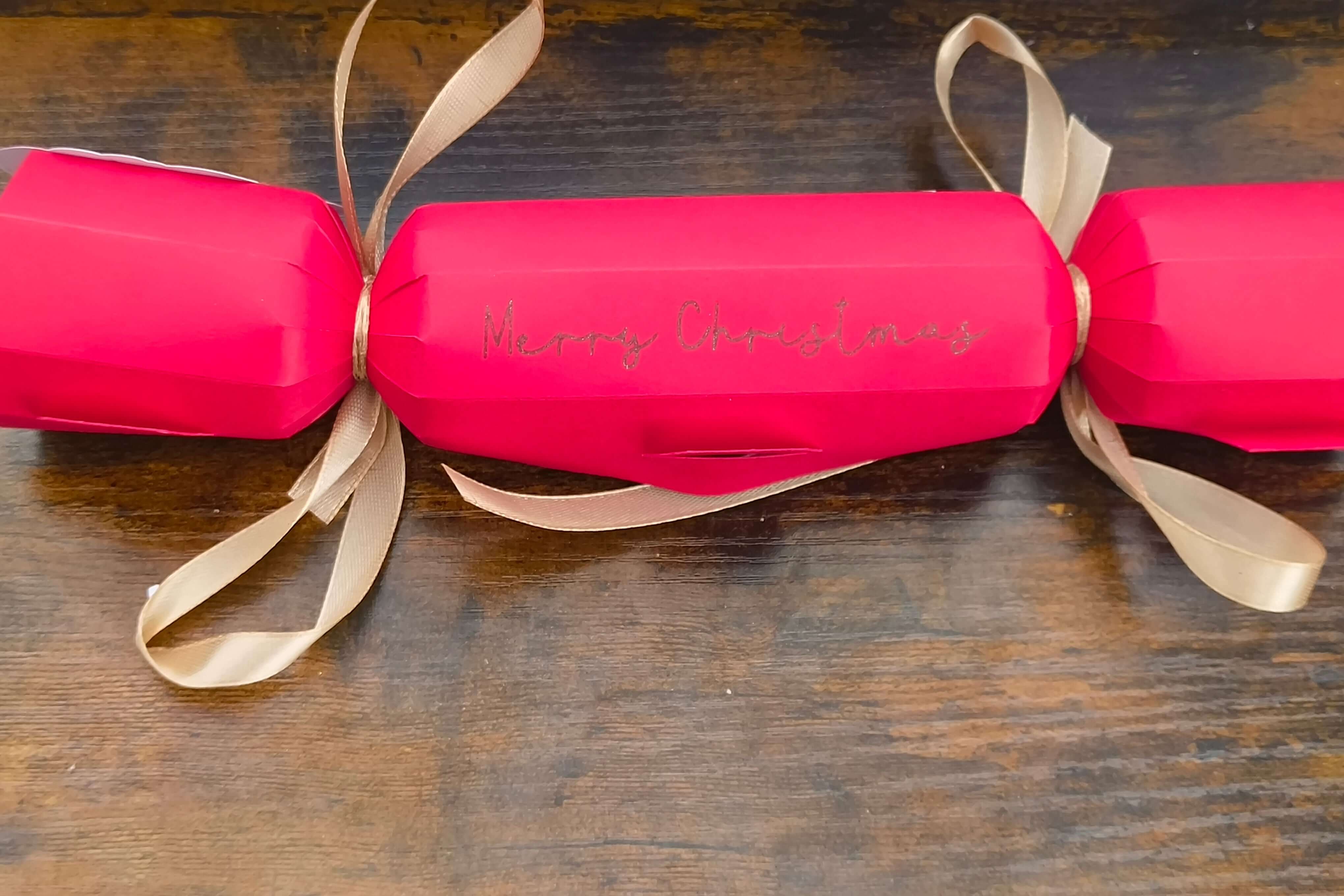 Personalised red Christmas cracker with gold ribbon and 'Merry Christmas' written on it.