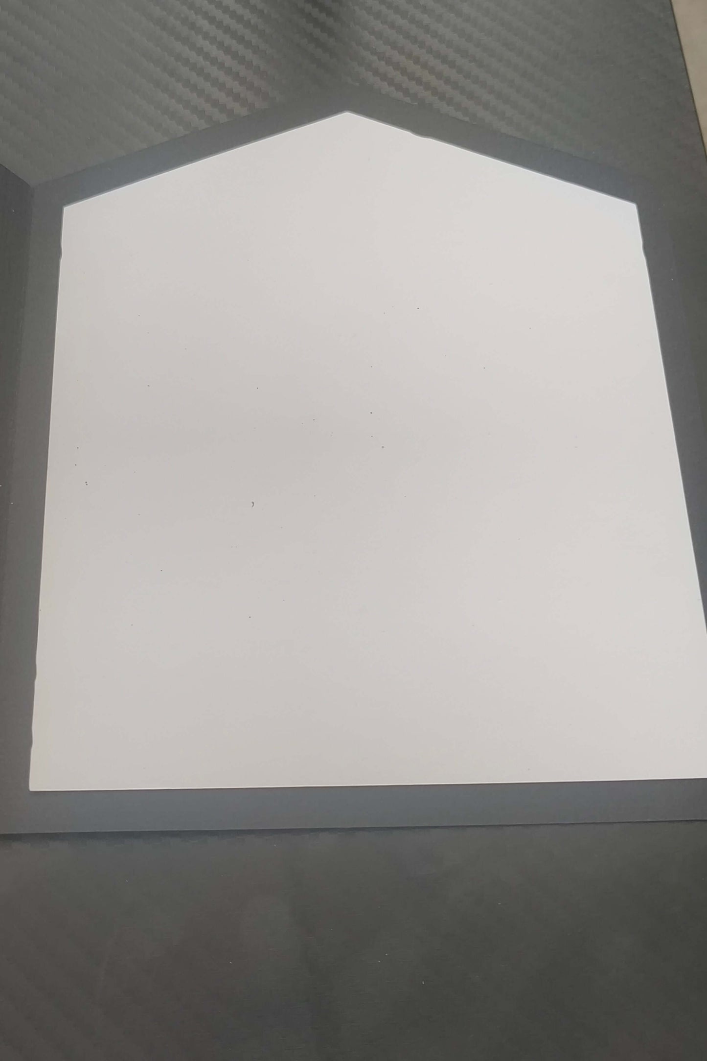 Blank folded card with a unique pentagon shape, placed on a textured black surface.