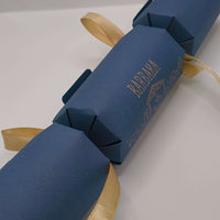 Luxury navy and gold handmade Christmas cracker shown at an angle, featuring Nativity design and satin ribbon ties.