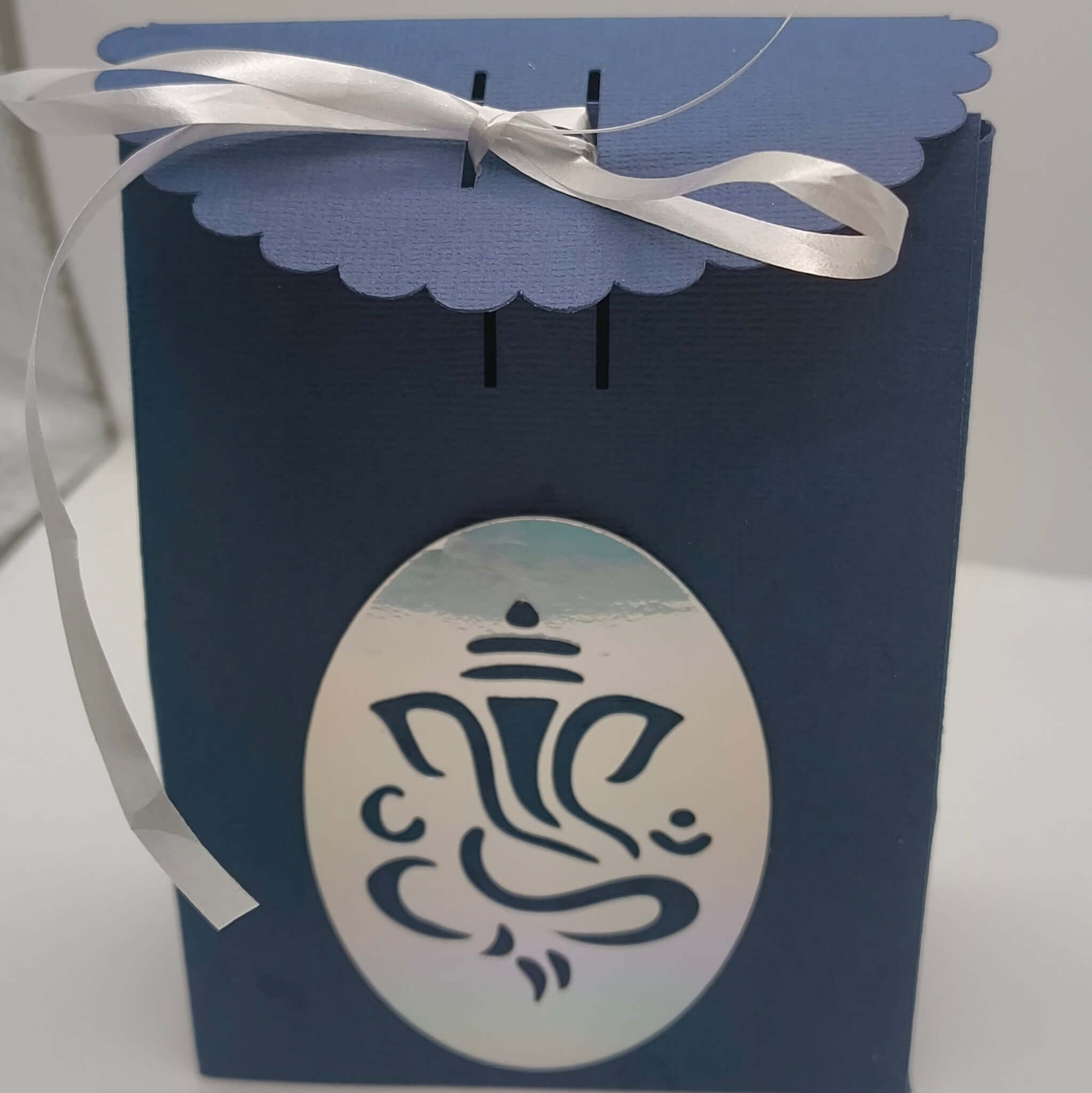 Handmade navy Hindu favour box with silver Ganesh design, scalloped lid and satin ribbon tie, perfect for Diwali or celebration treats.