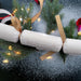 Handmade white New Year cracker with gold ribbon and “Happy New Year” lettering. Photographed with festive greenery, lights, and faux snow for a celebratory look.