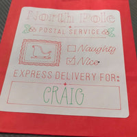 Red gift bag with a white label that reads 'North Pole Postal Service'. The label features checkboxes for 'Naughty' and 'Nice', with 'Nice' checked. Below it says 'Express Delivery For: CRAIG' in green and red festive fonts, with a sleigh icon and holly decorations.