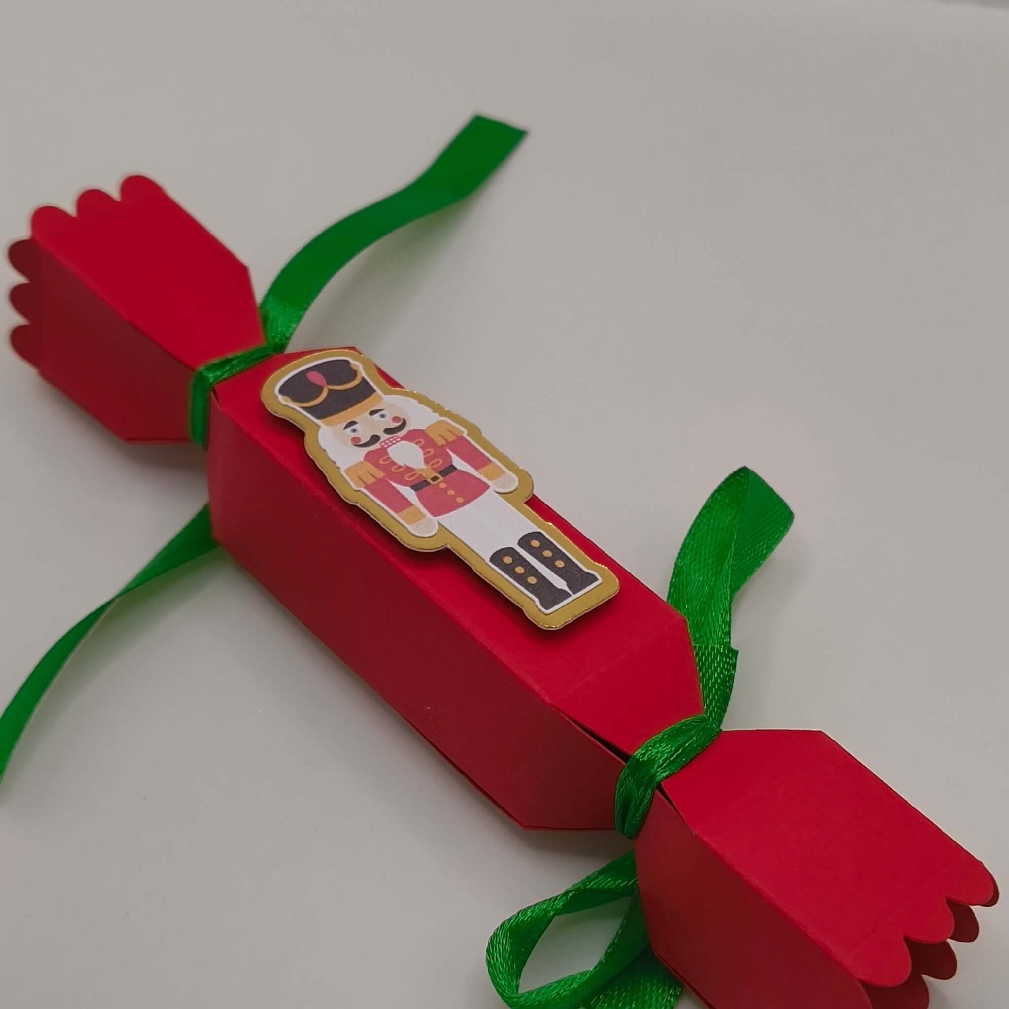 Angled view of the cracker, tied neatly with green satin ribbon. Shows the bold red card and decorative cut edges for a polished festive look.