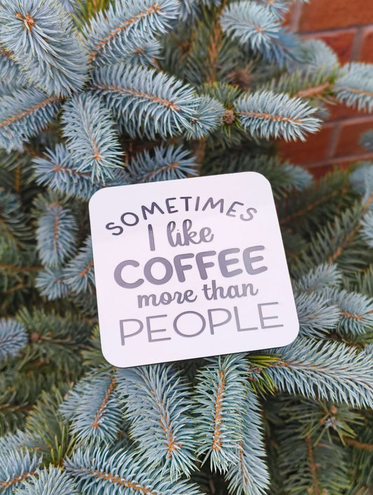 Funny coffee coaster gift with the phrase 'Sometimes I like coffee more than people' on a blue spruce background.