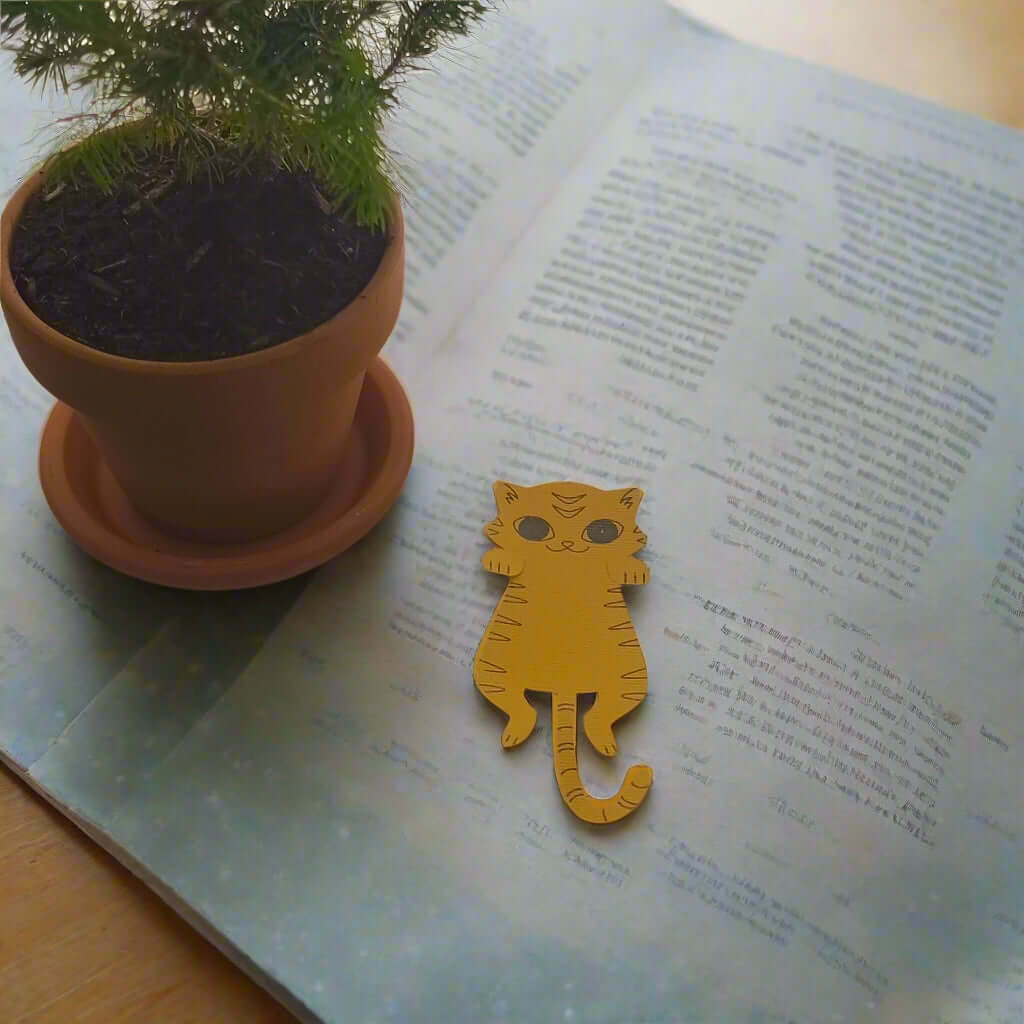 Flat lay of handmade orange cat bookmark on open book with plant in terracotta pot
