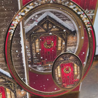 Close-up of oval topper on handmade Christmas card featuring a red door with wreath and golden embossed frame.