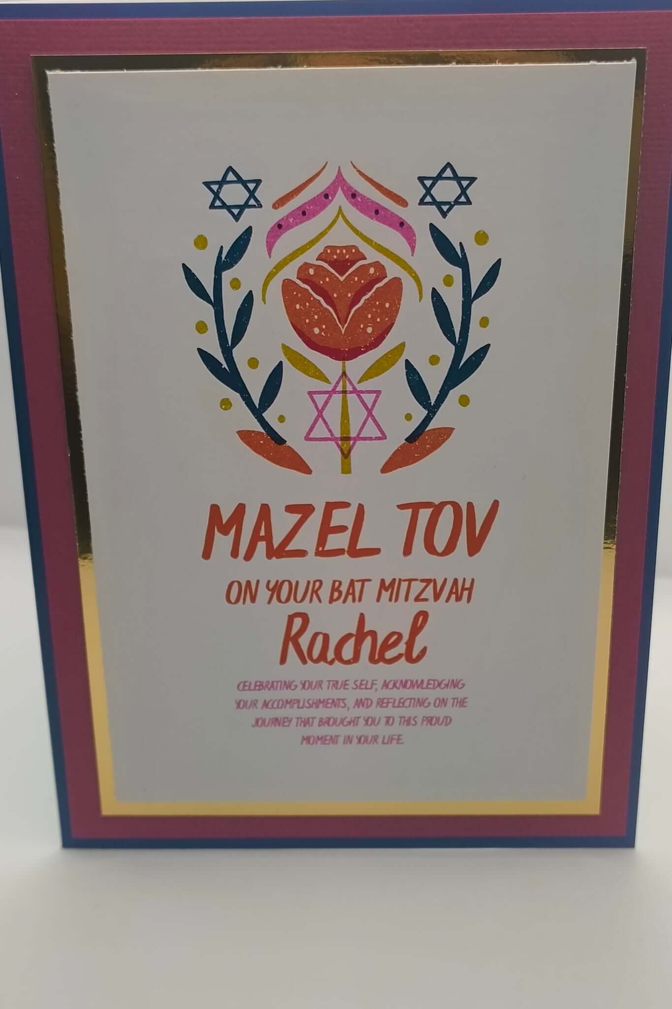 Close-up of Bat Mitzvah card with Mazel Tov message, floral Star of David design, and personalised name Rachel, finished with pink, blue, and gold foil layered cardstock.