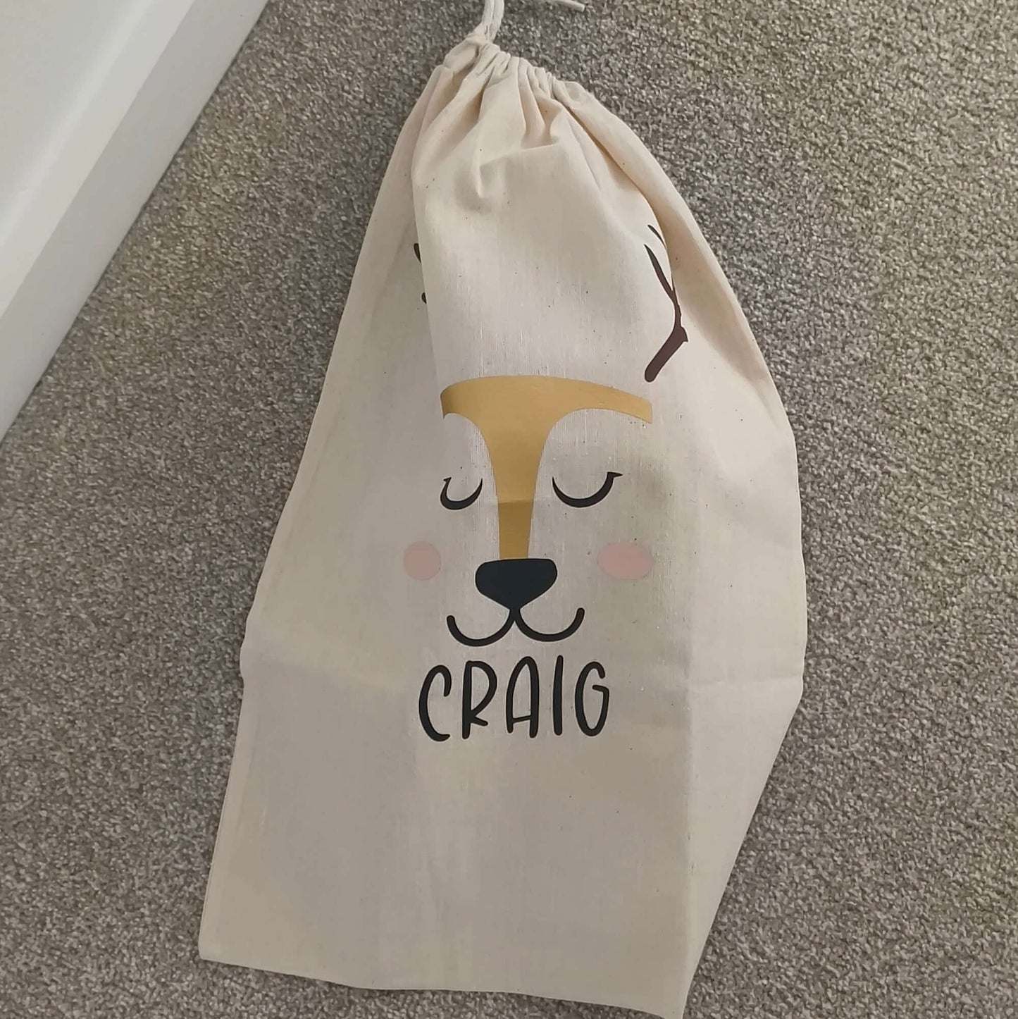 Personalised reindeer gift sack featuring a smiling reindeer face and the name 'Craig' in bold letters.