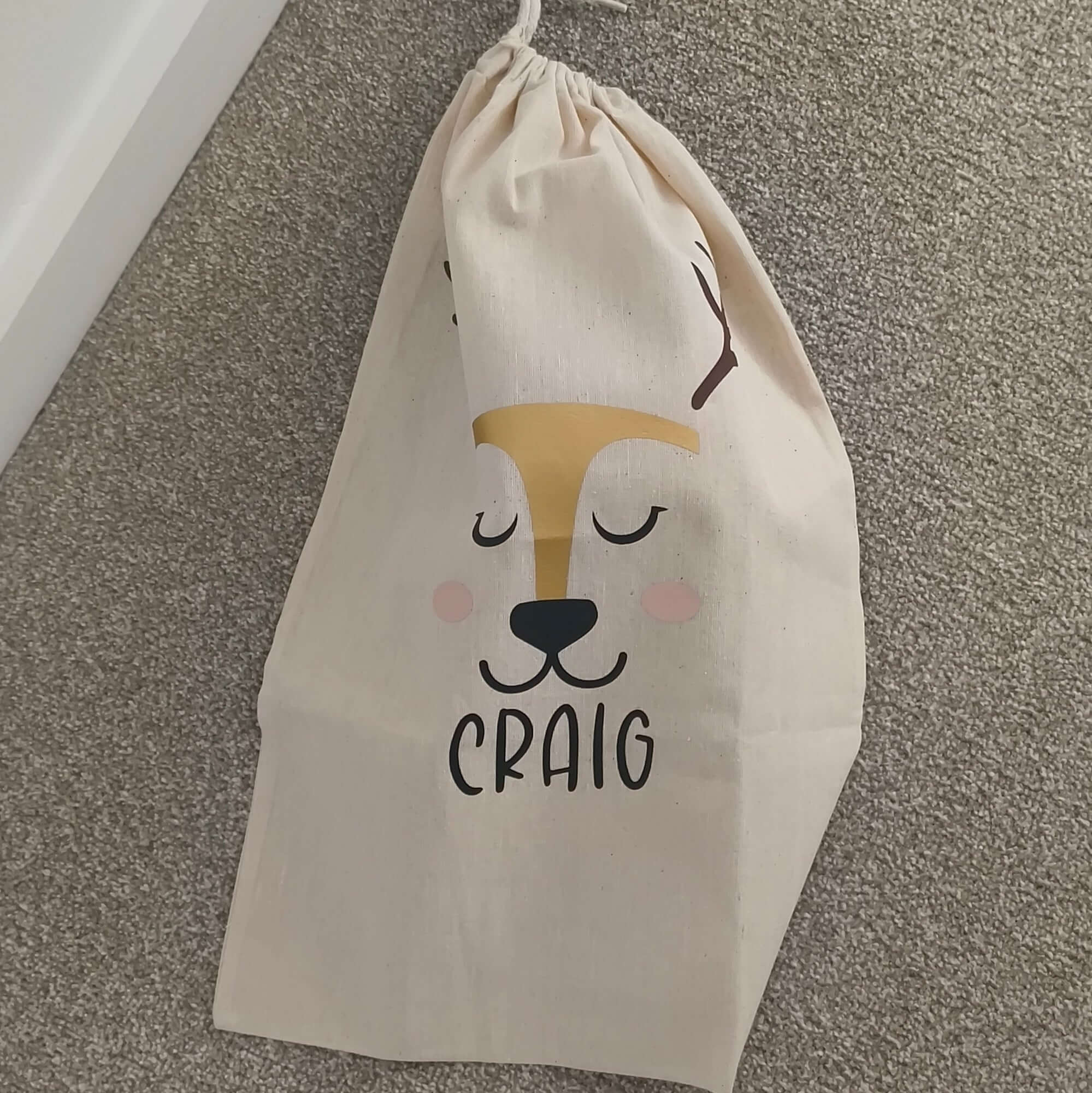 Personalised reindeer gift sack featuring a smiling reindeer face and the name 'Craig' in bold letters.