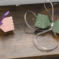 Pair of personalised crackers, one pink with “Penelope” and one green with “Craig,” styled with ribbons and a chocolate truffle for scale.