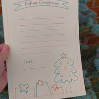 Close-up of Father Christmas letter writing paper held in hand with festive tree background.