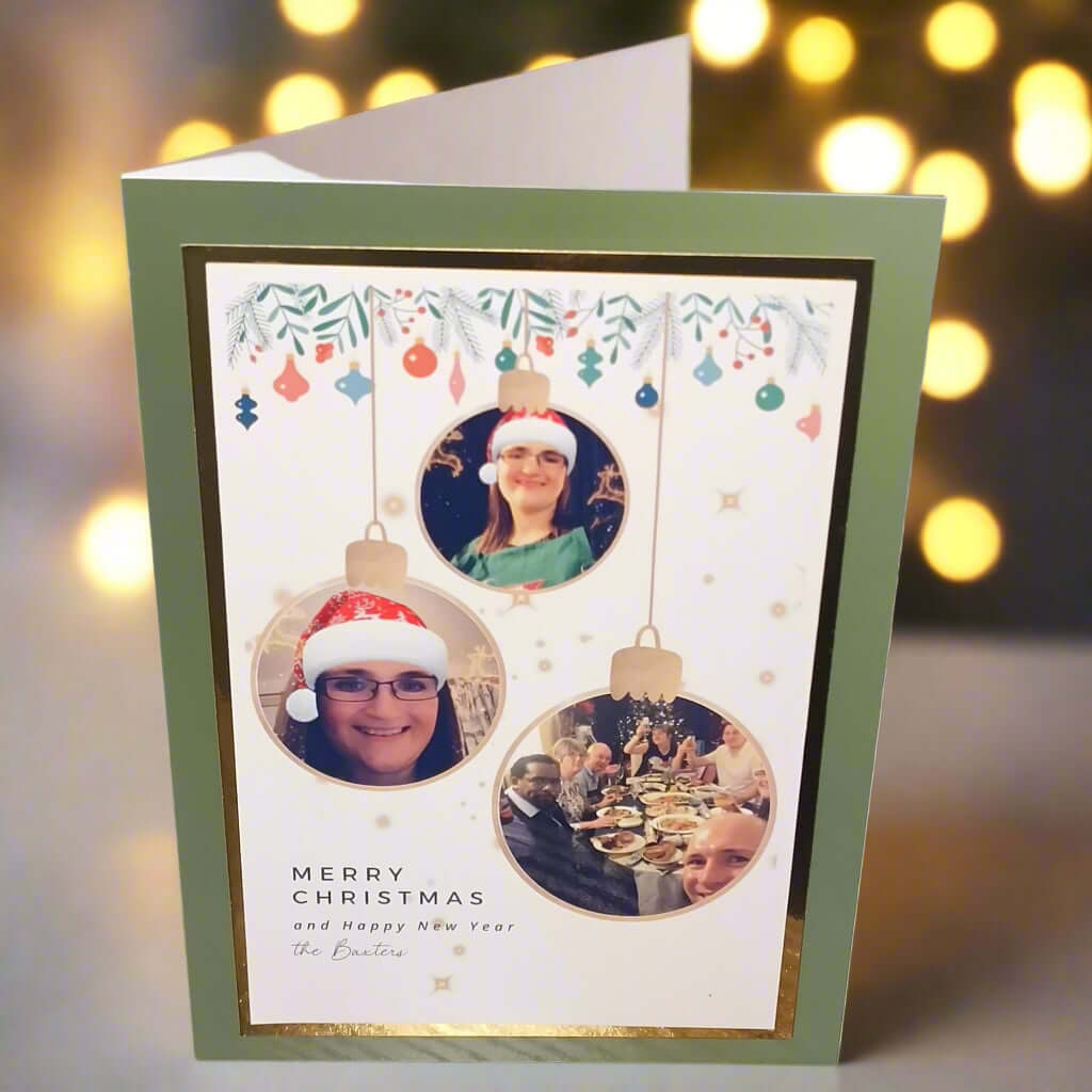 Personalised photo Christmas card – front angle view showing three bauble-style photo inserts with festive decorations and "Merry Christmas" message on a gold-trimmed green card.