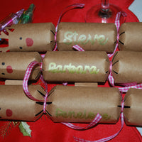 Set of handmade kraft reindeer crackers with red noses and names in gold lettering including Steve, Barbara, and Penelope, finished with pink gingham ribbon.