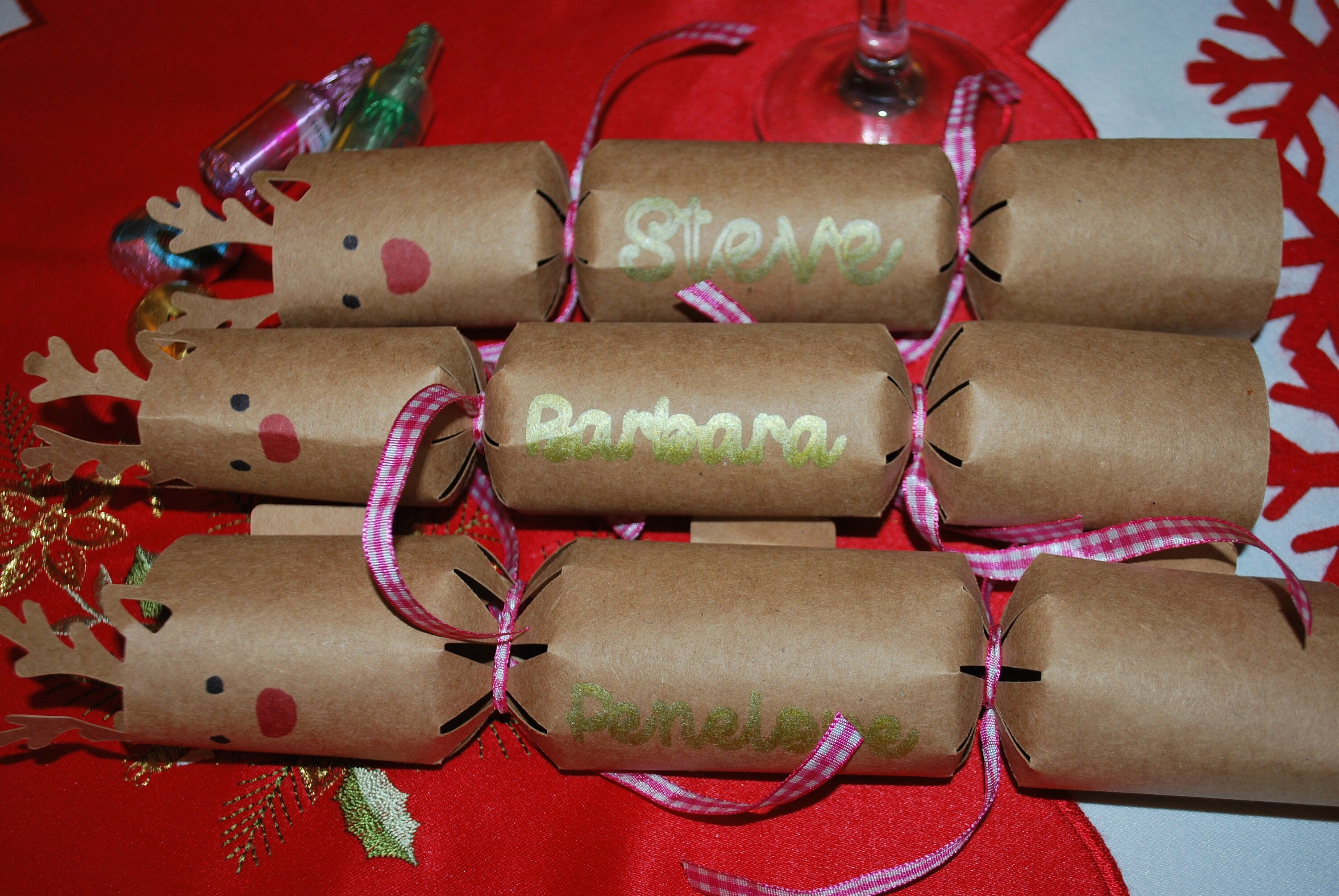 Set of handmade kraft reindeer crackers with red noses and names in gold lettering including Steve, Barbara, and Penelope, finished with pink gingham ribbon.