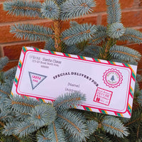 Personalised Santa delivery envelope resting on a Christmas tree with festive decorations and Santa's address.
