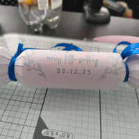 White wedding cracker with silver foil lettering and date, finished with bright blue-ribbon bows, placed on a cutting mat.
