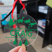 Clear acrylic dinosaur Christmas bauble with green vinyl, personalised with the name Craig, Santa in sleigh pulled by dinosaurs.