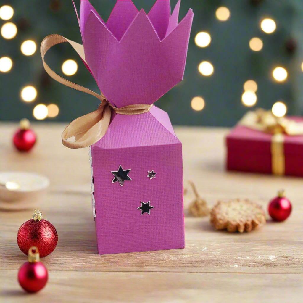 Handmade pink Christmas cracker box with snowflake design and shiny stars, decorated for festive celebrations.