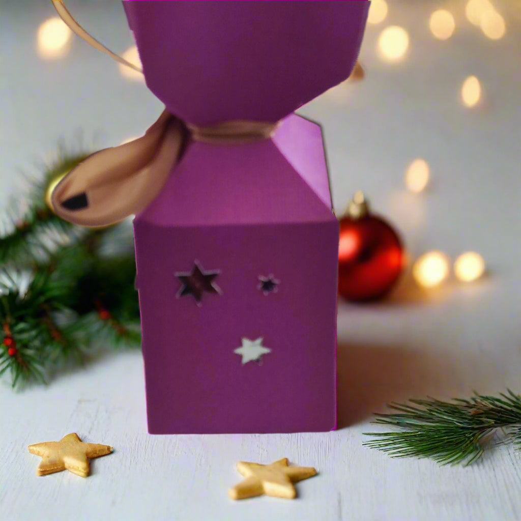 Handmade pink Christmas cracker box with star cutouts, festive decorations, and holiday lights in the background.