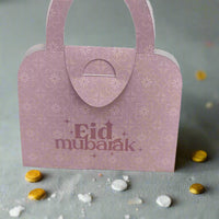 Light pink Eid Mubarak money holder with floral print, handbag design, surrounded by festive coins, perfect for Eid gifts.