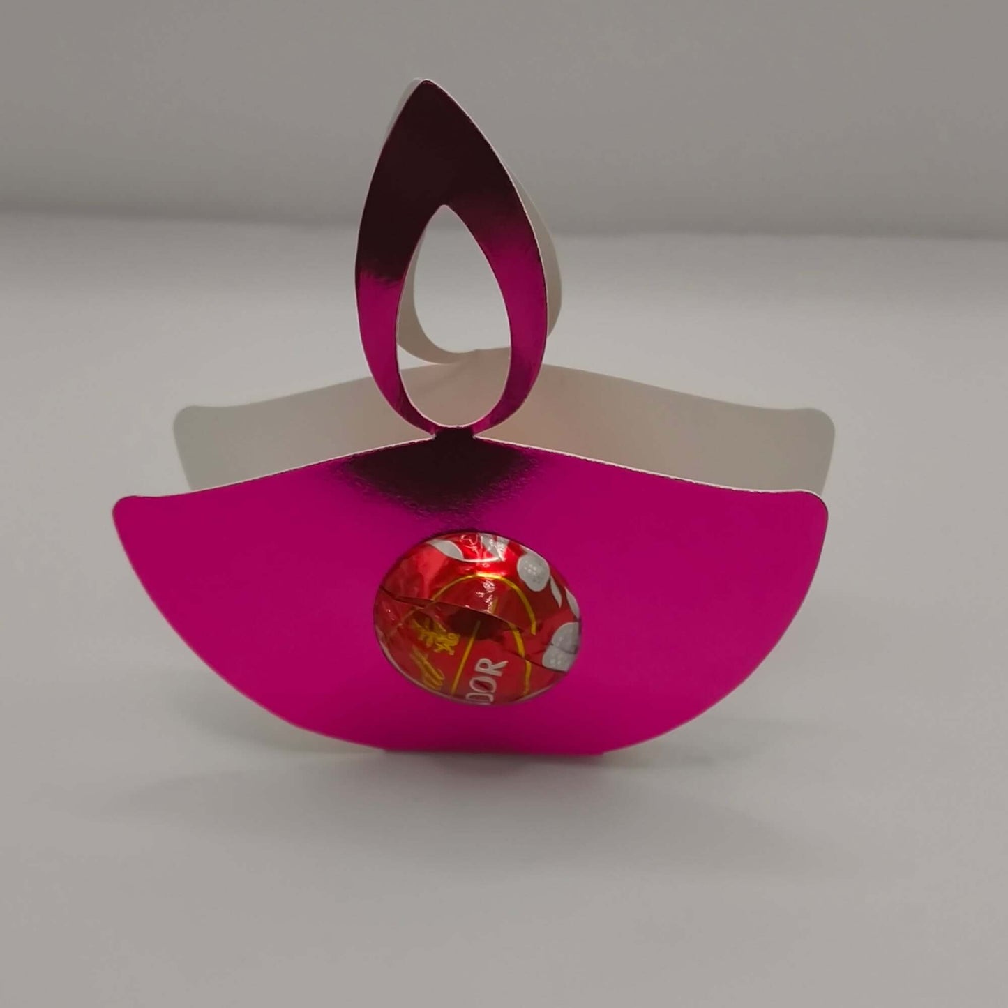 Pink metallic diya favour holding a chocolate, perfect for Diwali celebrations and party gifts.