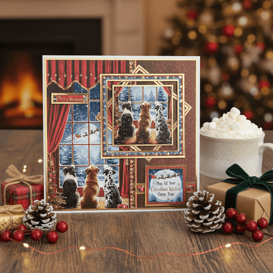 Decorative Christmas card with dogs by a window, surrounded by festive items like a mug of hot chocolate and pine cones.