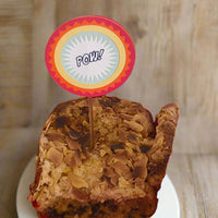 Front-facing view of comic-style 'POW!' cake topper inserted into an almond-topped loaf cake, designed for superhero-themed parties.