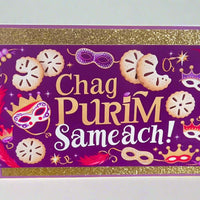 Front-facing handmade Chag Purim Sameach card with gold glitter borders, purple background, hamantaschen and mask illustrations, close-up detail on plain light backdrop