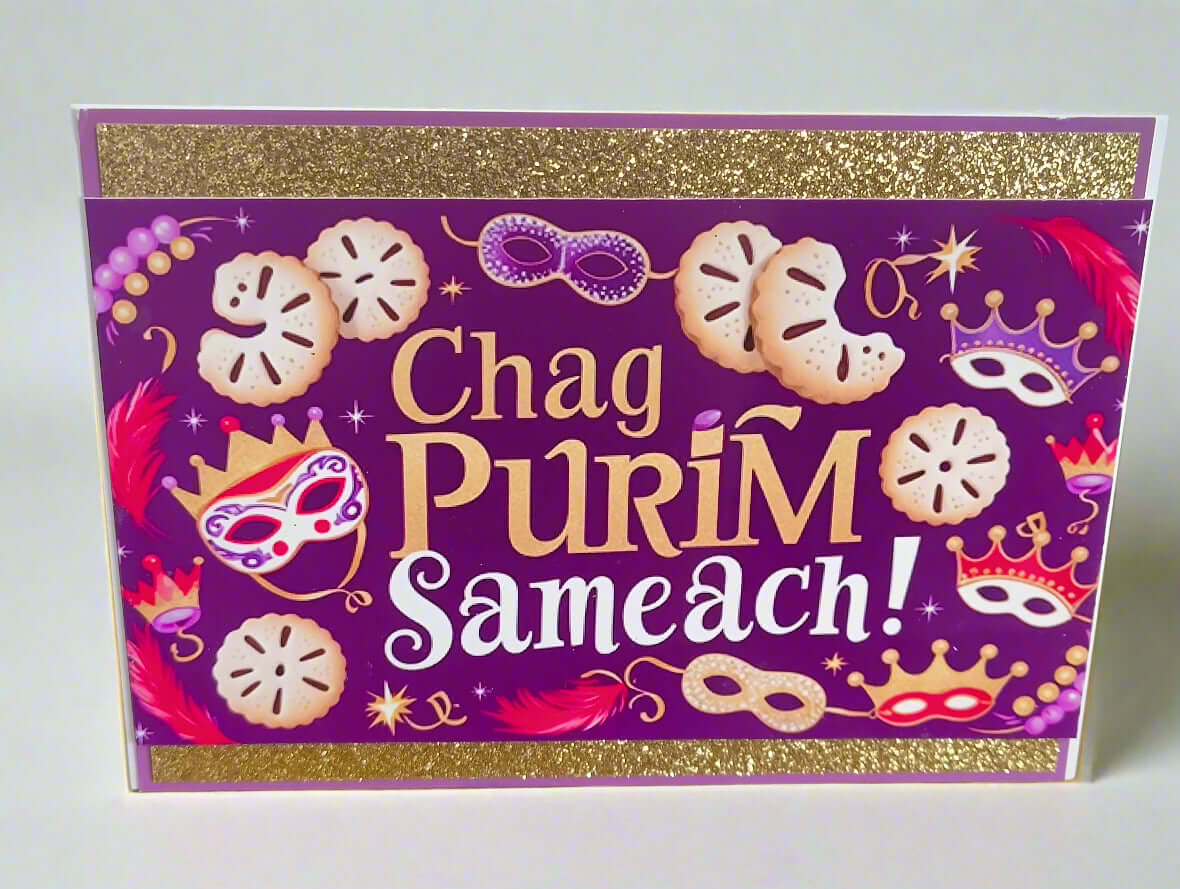 Front-facing handmade Chag Purim Sameach card with gold glitter borders, purple background, hamantaschen and mask illustrations, close-up detail on plain light backdrop