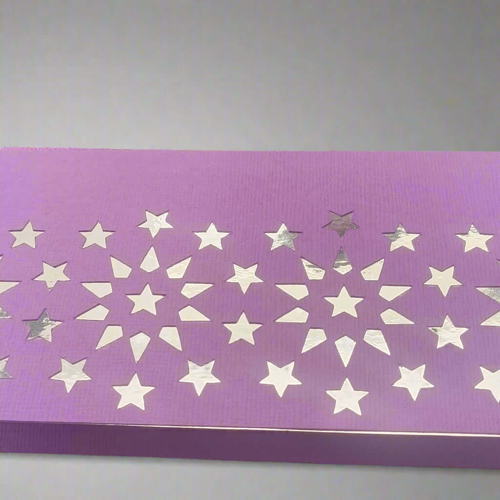 Close-up view of a handmade purple money holder featuring a silver foiled starburst pattern on textured cardstock, set against a soft grey background.