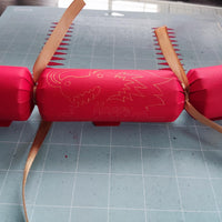 Handmade red Chinese New Year cracker with gold foil dragon design, tied with gold ribbon, shown flat on a crafting mat during assembly.