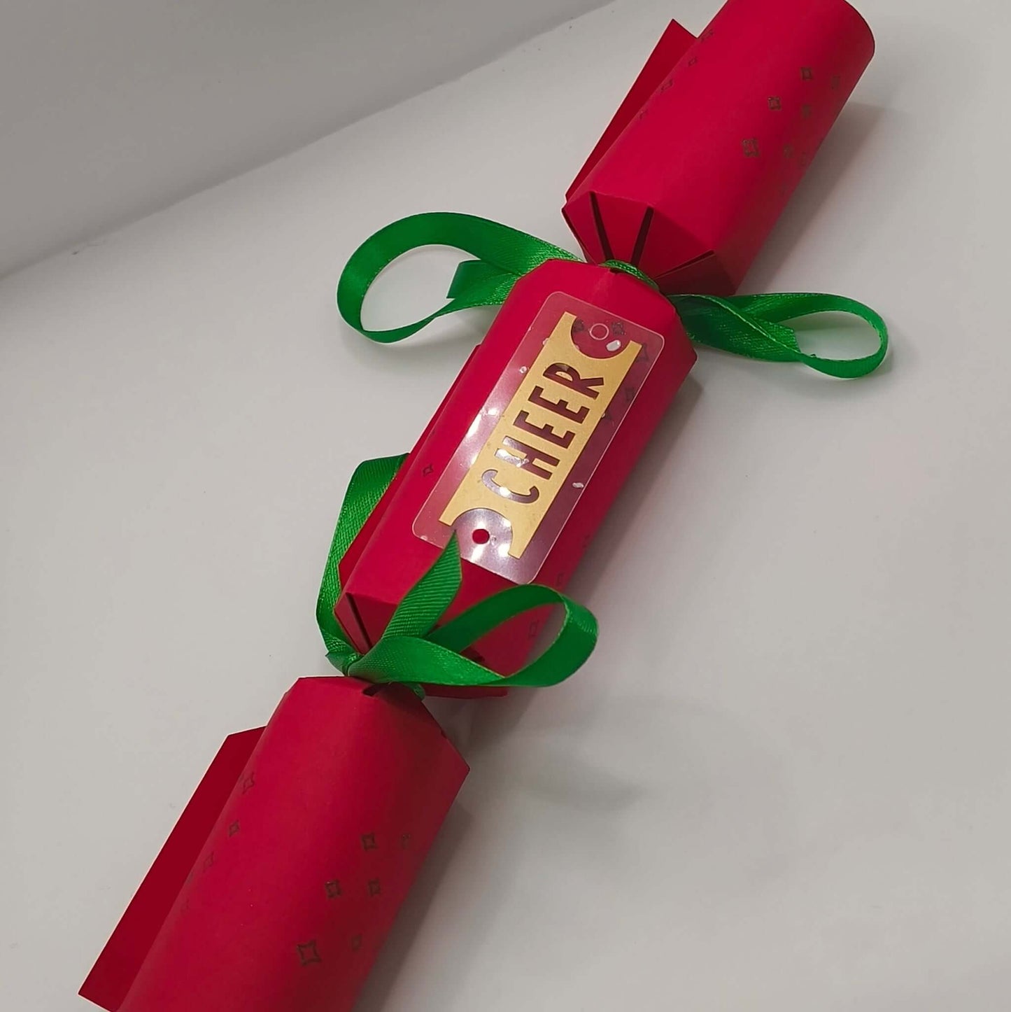 Red Christmas cracker with green ribbon and gold ‘CHEER’ tag, displayed on a white background.