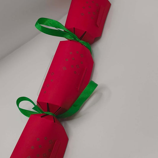 Red handmade Christmas cracker with green ribbon bows and embossed star pattern.