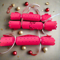 Set of red handmade Christmas crackers with silver ribbon ties and cut-out dot design. Shown with festive baubles for scale.
