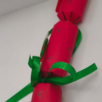 Side view of red cracker with green satin ribbon and silver holly print design.