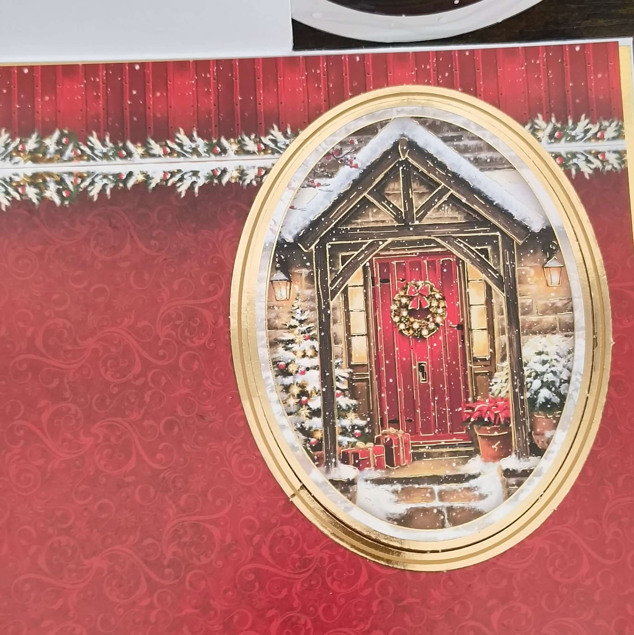 Handmade Christmas card base with gold border and red patterned background featuring snowy red door cottage design.