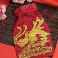 Red hessian gift bag with gold glitter dragon design and “Happy Chinese New Year” text, styled with cherry blossoms.