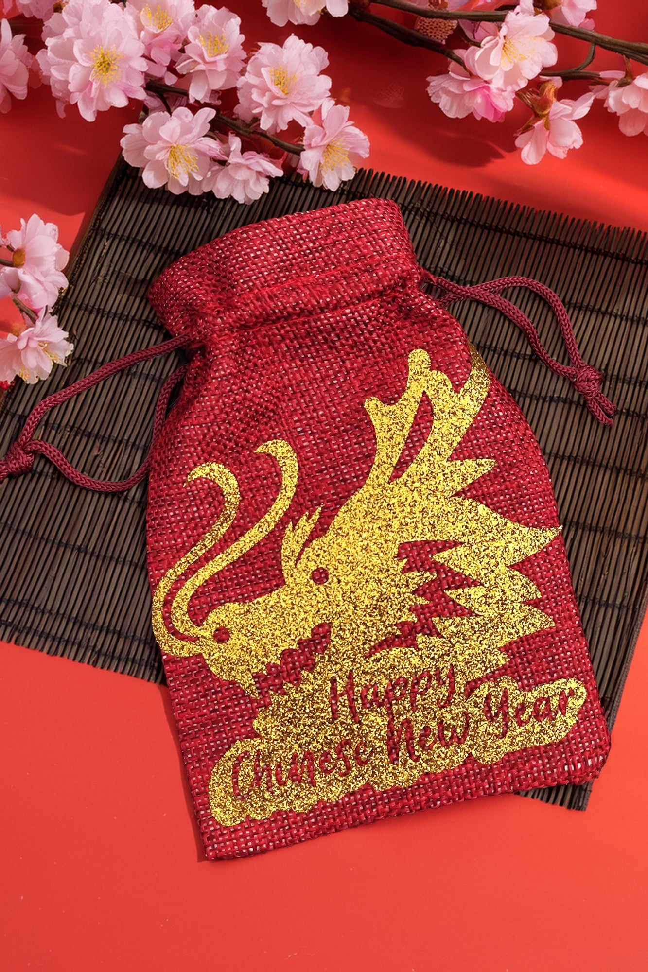 Red hessian gift bag with gold glitter dragon design and “Happy Chinese New Year” text, styled with cherry blossoms.