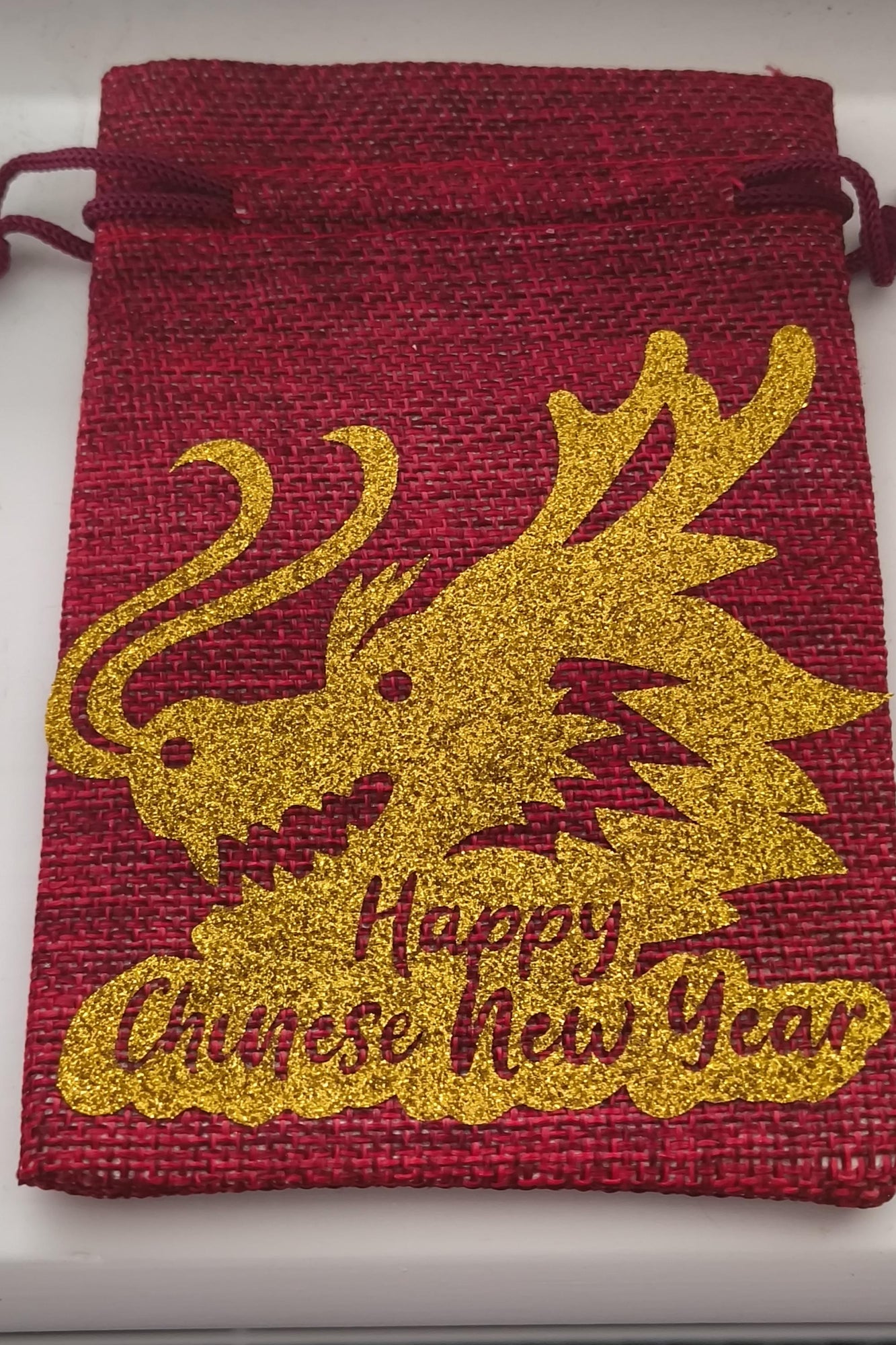 Red hessian Chinese New Year drawstring bag with sparkling gold dragon print and festive message.